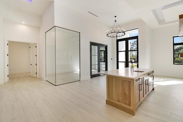 kitchen with light hardwood / wood-style floors, a kitchen island with sink, french doors, pendant lighting, and sink