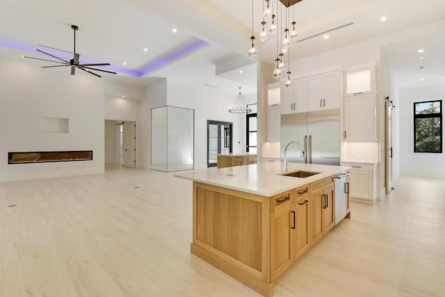 kitchen with sink, stainless steel built in fridge, a large island, white cabinets, and ceiling fan with notable chandelier