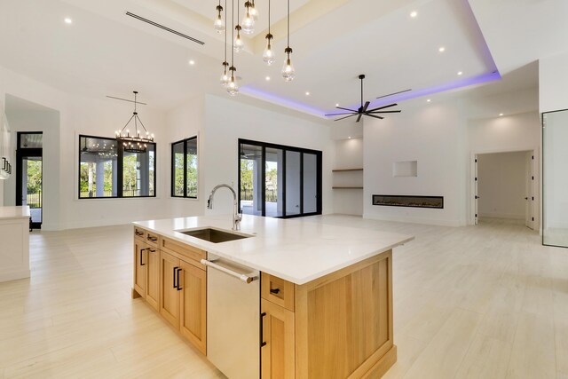 kitchen featuring a tray ceiling, light brown cabinets, sink, a large island, and stainless steel dishwasher