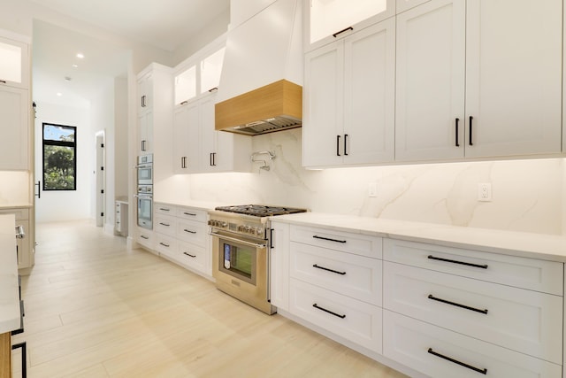 kitchen featuring backsplash, white cabinets, stainless steel appliances, and custom exhaust hood