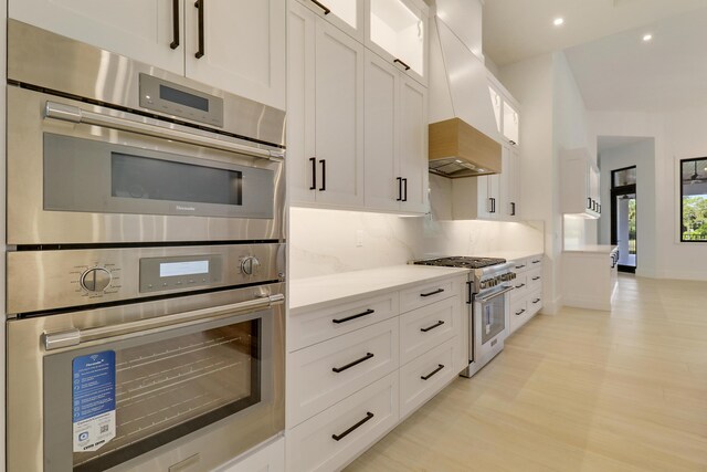 kitchen with premium range hood, white cabinetry, appliances with stainless steel finishes, light hardwood / wood-style floors, and backsplash