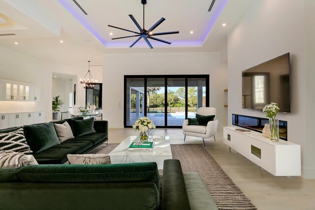 living room featuring ceiling fan with notable chandelier, a tray ceiling, and light hardwood / wood-style flooring