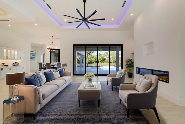 living room with ceiling fan with notable chandelier, wood-type flooring, and a tray ceiling