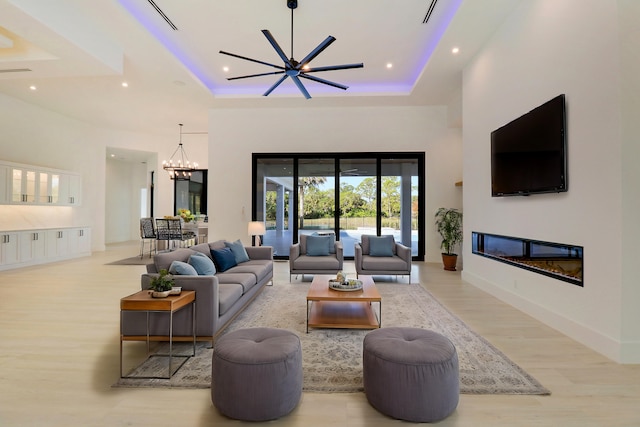 living room featuring a raised ceiling, light wood-type flooring, and ceiling fan with notable chandelier