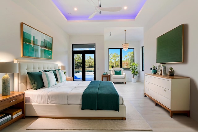 bedroom featuring ceiling fan, access to exterior, a tray ceiling, and light hardwood / wood-style flooring