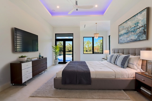 bedroom with a raised ceiling, light colored carpet, access to exterior, and ceiling fan