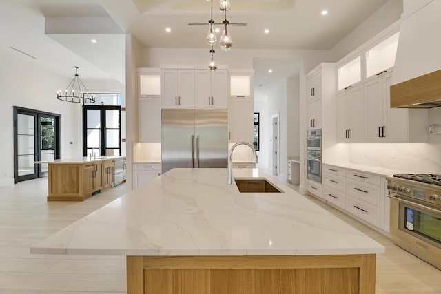 kitchen with hanging light fixtures, high end appliances, white cabinets, and a spacious island