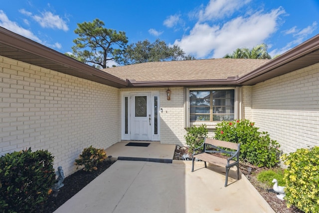 entrance to property featuring a shingled roof and brick siding