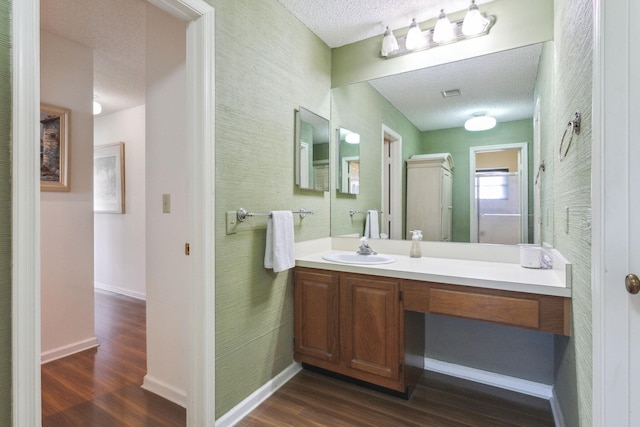 bathroom featuring visible vents, baseboards, wood finished floors, a textured ceiling, and vanity