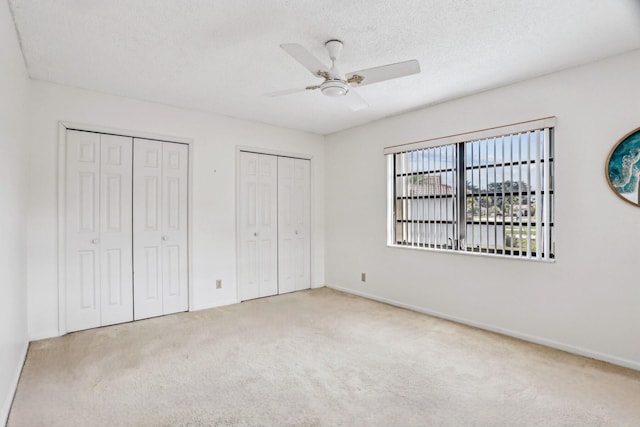 unfurnished bedroom with baseboards, ceiling fan, a textured ceiling, carpet floors, and multiple closets