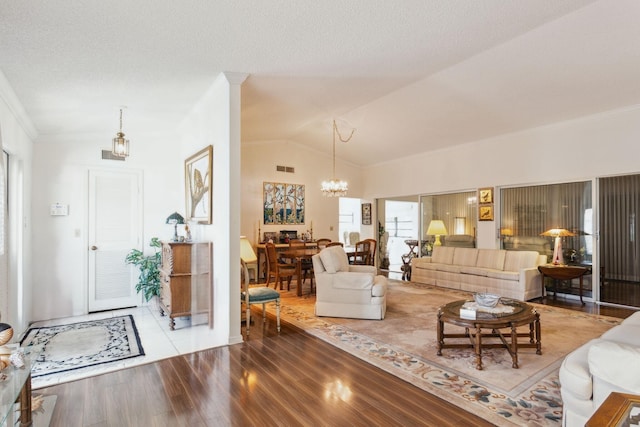 living area with crown molding, an inviting chandelier, vaulted ceiling, a textured ceiling, and wood finished floors