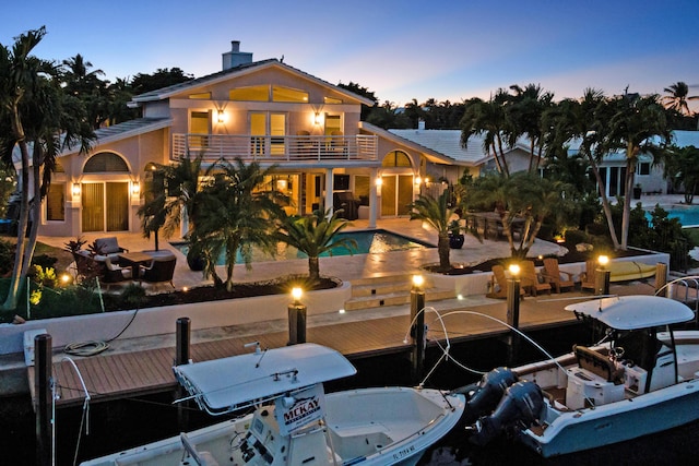 back house at dusk featuring a balcony and a patio area