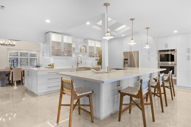 kitchen featuring appliances with stainless steel finishes, a skylight, sink, white cabinetry, and a large island