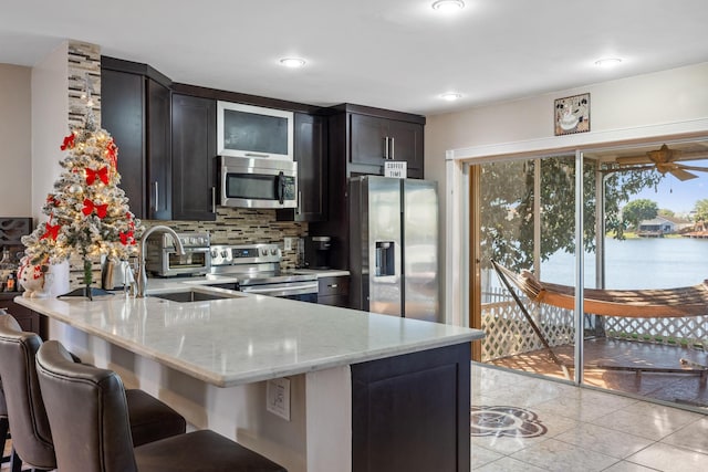 kitchen featuring kitchen peninsula, appliances with stainless steel finishes, backsplash, light stone counters, and a water view