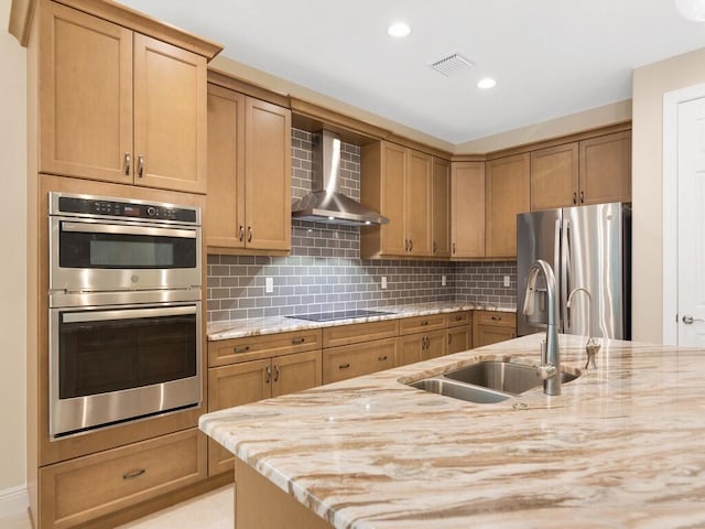 kitchen with sink, stainless steel appliances, wall chimney range hood, tasteful backsplash, and light stone counters