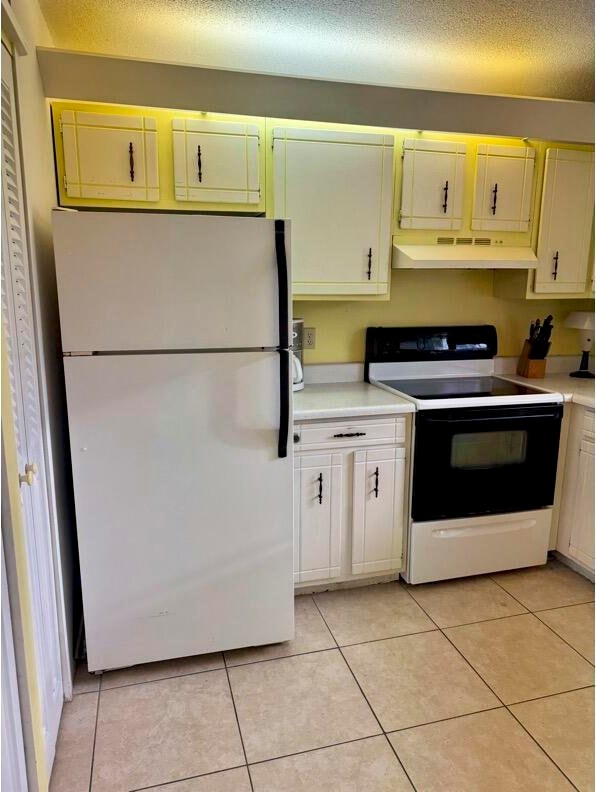 kitchen with a textured ceiling, white cabinets, light tile patterned floors, and white appliances