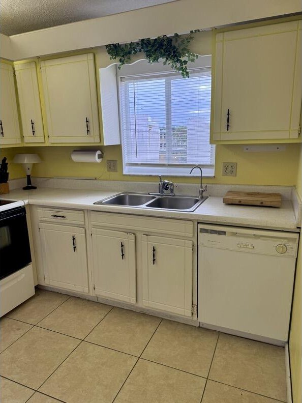 kitchen with a textured ceiling, white appliances, sink, and light tile patterned floors