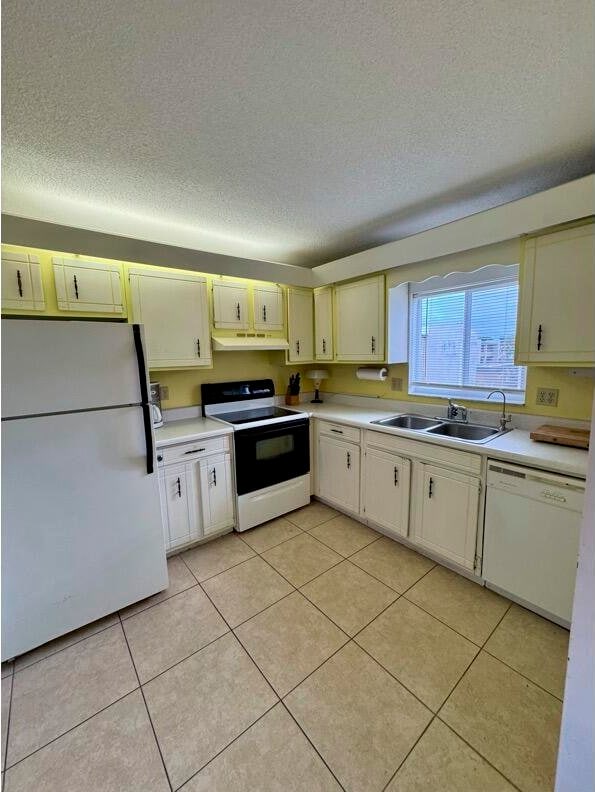 kitchen featuring a textured ceiling, white appliances, sink, and light tile patterned floors