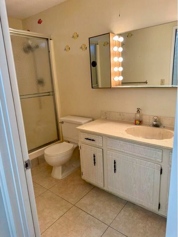 bathroom with tile patterned flooring, vanity, an enclosed shower, and toilet