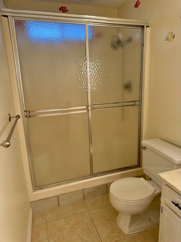 bathroom featuring toilet, vanity, tile patterned floors, and a shower with door