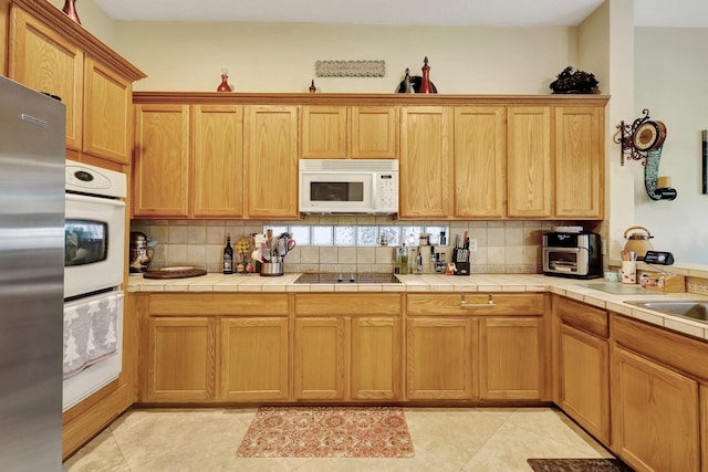 kitchen featuring tile countertops, stainless steel fridge, black electric cooktop, decorative backsplash, and light tile patterned flooring