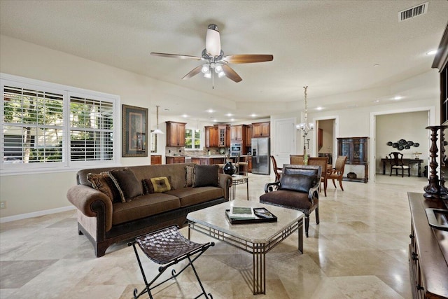 living room featuring ceiling fan with notable chandelier and a textured ceiling