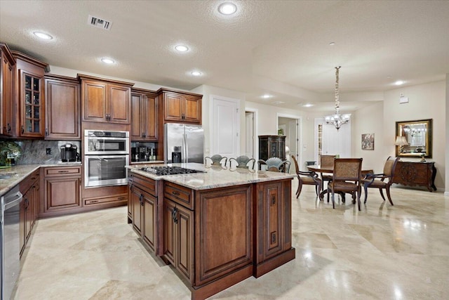 kitchen with pendant lighting, a kitchen island, a textured ceiling, and appliances with stainless steel finishes