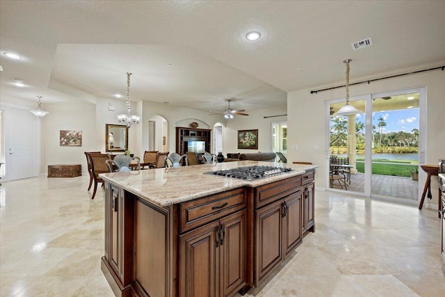 kitchen featuring stainless steel gas stovetop, ceiling fan with notable chandelier, a textured ceiling, decorative light fixtures, and a kitchen island