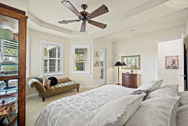 bedroom featuring ceiling fan, light colored carpet, a textured ceiling, and a tray ceiling