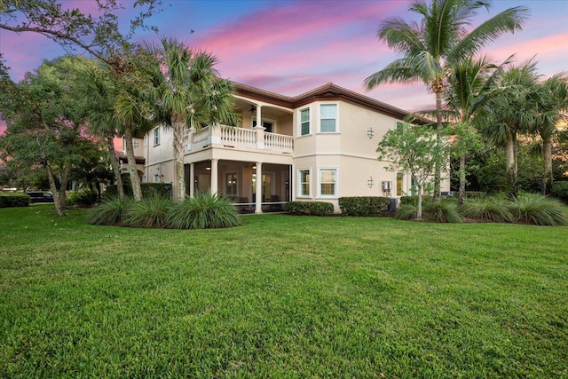 back house at dusk with a balcony and a yard