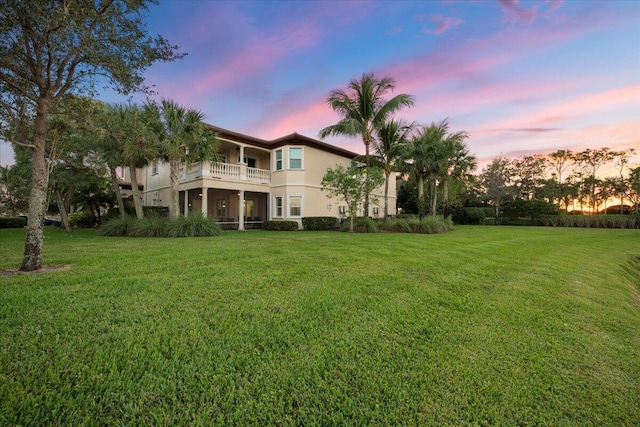 back house at dusk featuring a yard and a balcony