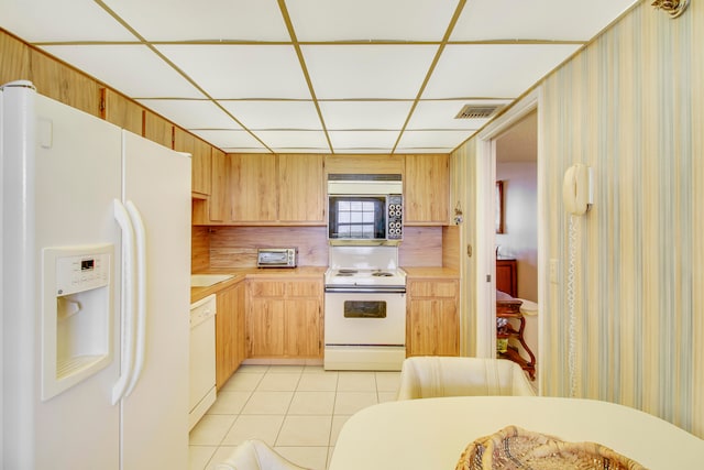 kitchen with a drop ceiling, light tile patterned floors, white appliances, and light brown cabinetry