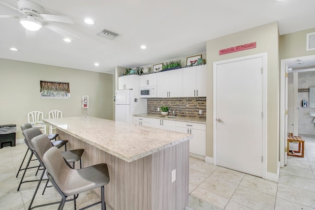 kitchen featuring white cabinetry, a center island, white appliances, a kitchen bar, and light tile patterned flooring