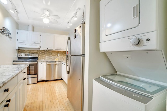 kitchen featuring appliances with stainless steel finishes, stacked washer and dryer, extractor fan, and white cabinetry