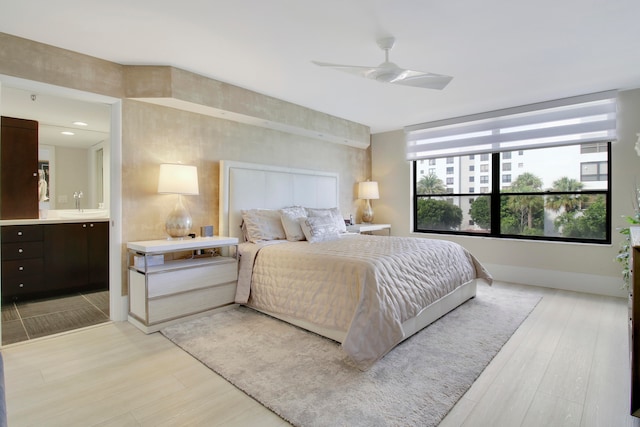 bedroom featuring light wood-type flooring, ensuite bathroom, ceiling fan, and sink