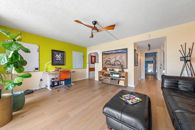 living room with ceiling fan, light wood-type flooring, and a textured ceiling