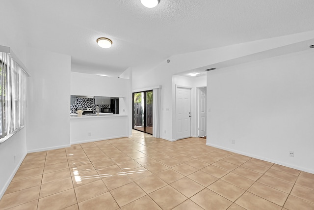 unfurnished living room featuring light tile patterned flooring, lofted ceiling, and a textured ceiling