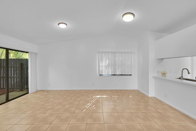 unfurnished room with a textured ceiling, light tile patterned flooring, lofted ceiling, and sink