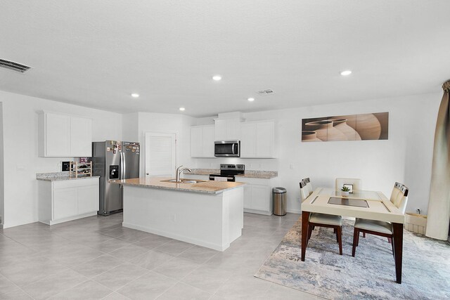 kitchen featuring light stone countertops, stainless steel appliances, a kitchen island with sink, sink, and white cabinetry