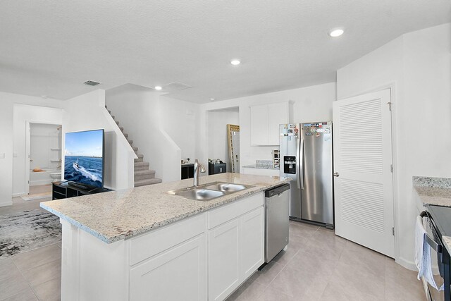 kitchen with white cabinetry, sink, stainless steel appliances, a textured ceiling, and a center island with sink