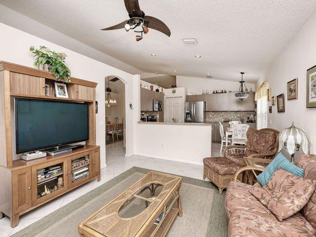 living room featuring ceiling fan with notable chandelier, light tile patterned floors, a textured ceiling, and lofted ceiling