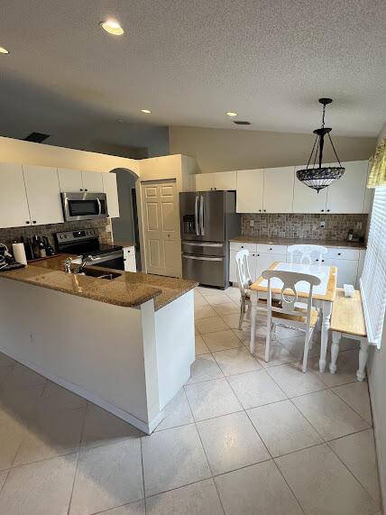 kitchen with kitchen peninsula, decorative backsplash, stainless steel appliances, pendant lighting, and white cabinetry