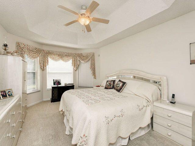 bedroom with ceiling fan, light colored carpet, a textured ceiling, and a tray ceiling