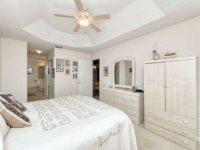 bedroom featuring light colored carpet, ceiling fan, a tray ceiling, and ensuite bathroom