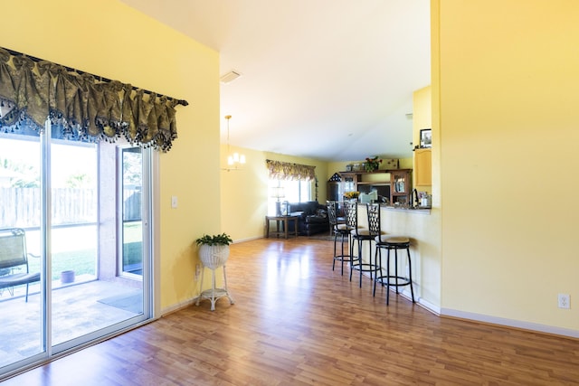 kitchen with hardwood / wood-style floors, a breakfast bar, lofted ceiling, kitchen peninsula, and a chandelier