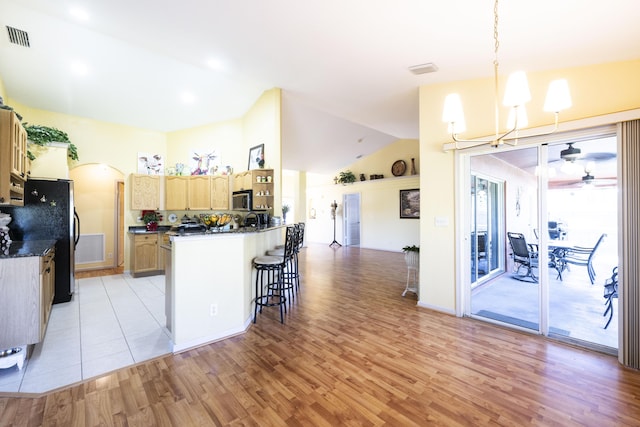 kitchen with black fridge, light hardwood / wood-style flooring, kitchen peninsula, lofted ceiling, and ceiling fan with notable chandelier