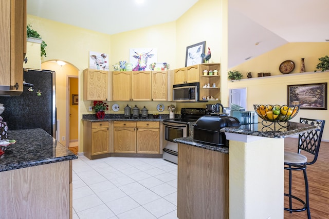 kitchen featuring kitchen peninsula, black refrigerator, electric range oven, a breakfast bar area, and lofted ceiling