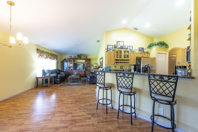 kitchen featuring stainless steel refrigerator with ice dispenser, vaulted ceiling, light hardwood / wood-style flooring, a kitchen bar, and kitchen peninsula