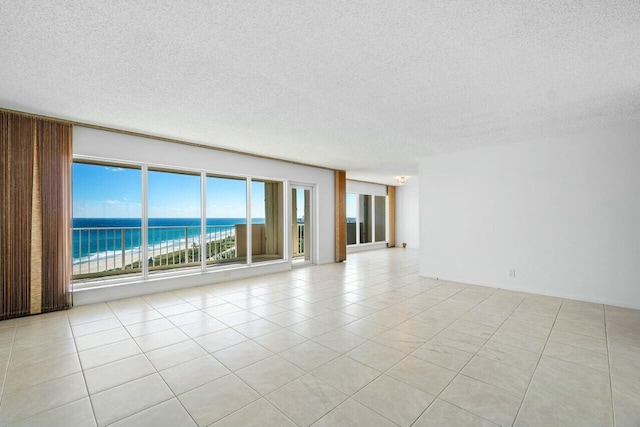 spare room featuring light tile patterned floors, a water view, a view of the beach, and a textured ceiling