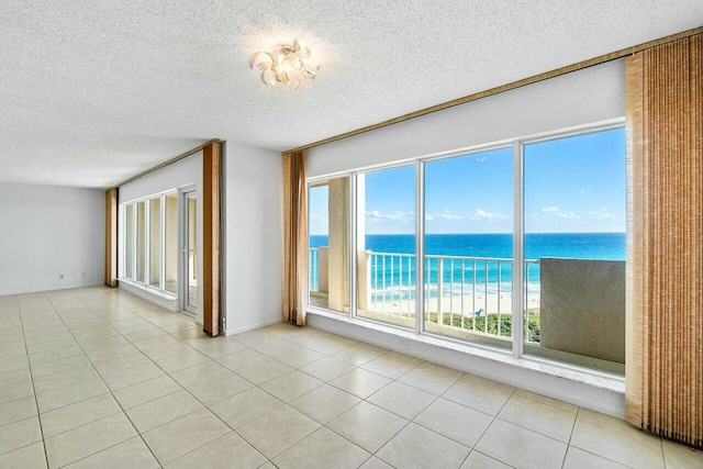 unfurnished room with a water view, light tile patterned floors, and a textured ceiling